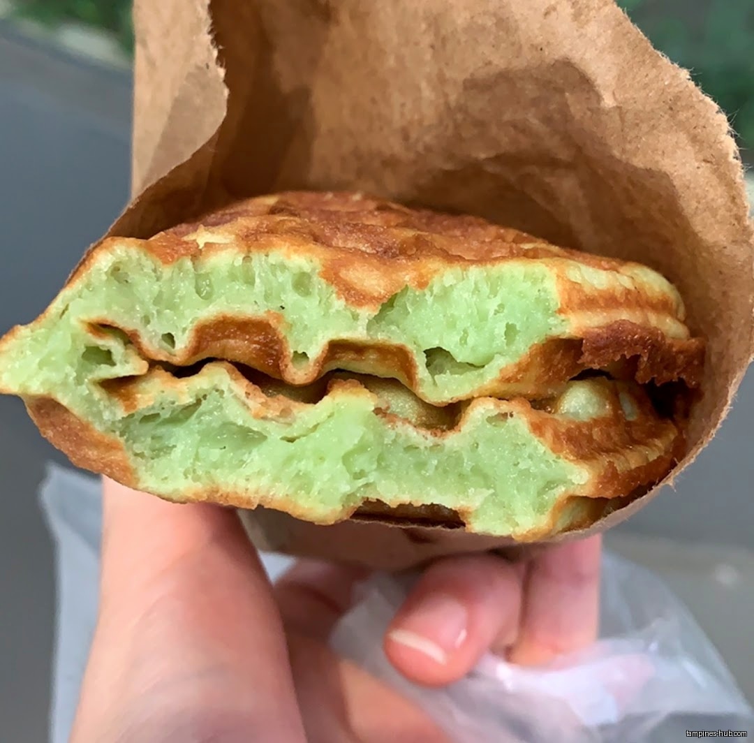 A green waffle-like pastry from KenJinn Bakery is held in a paper bag.