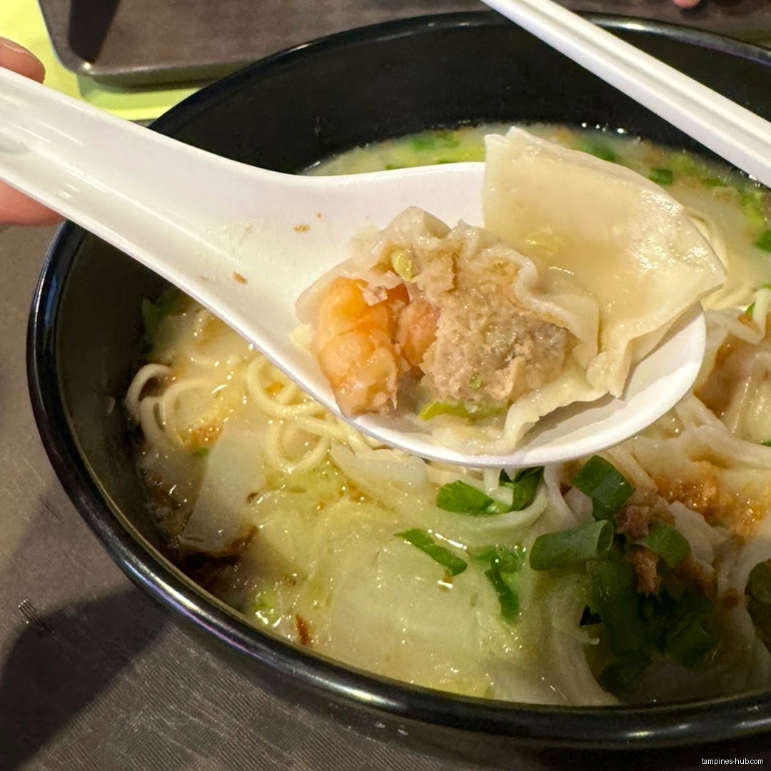 A bowl of noodles with dumplings and a spoon holding a dumpling.