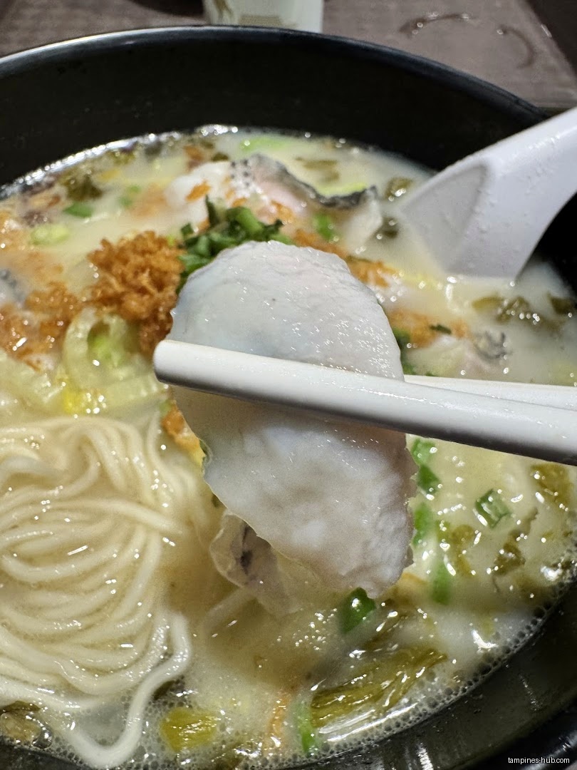 Close-up of noodles and fish in broth, held by chopsticks.