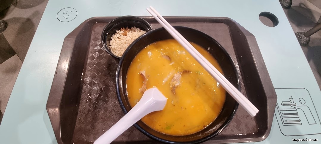 A tray with a bowl of soup, rice, spoon, and chopsticks.