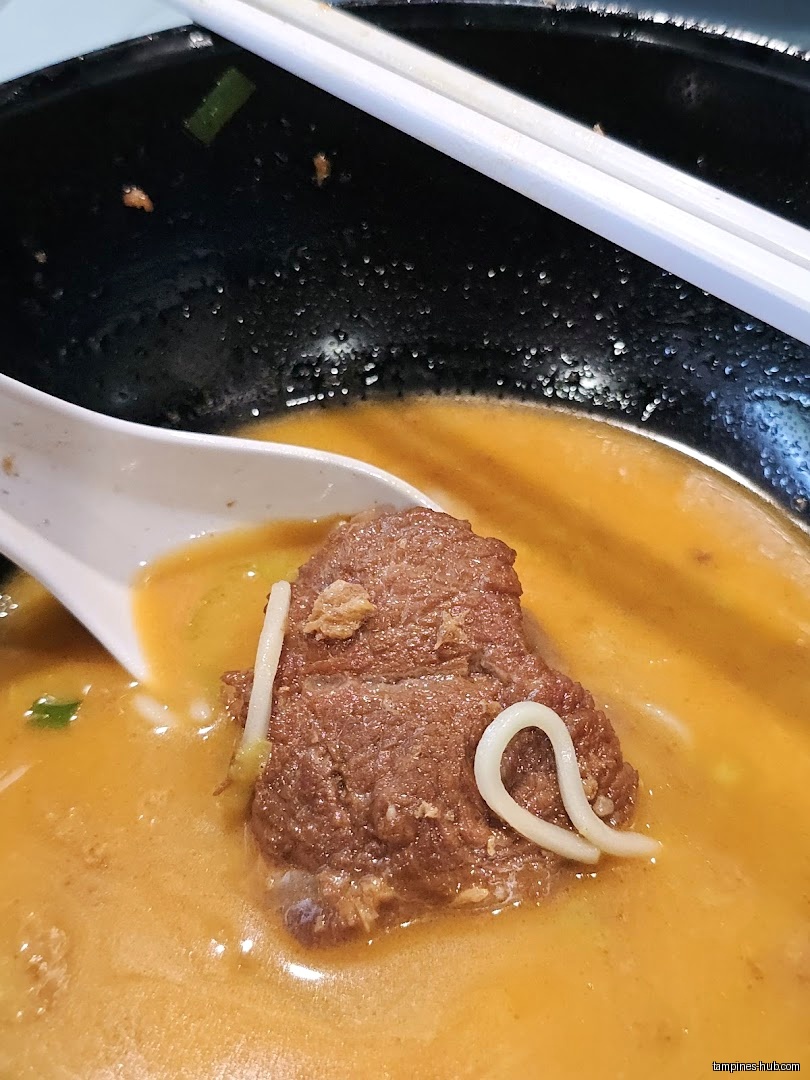 Close-up of a spoon holding meat in a bowl of soup.