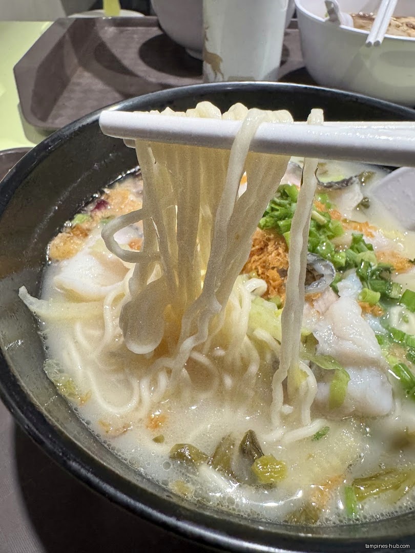 Close-up of noodles and fish in a creamy broth, held by chopsticks.