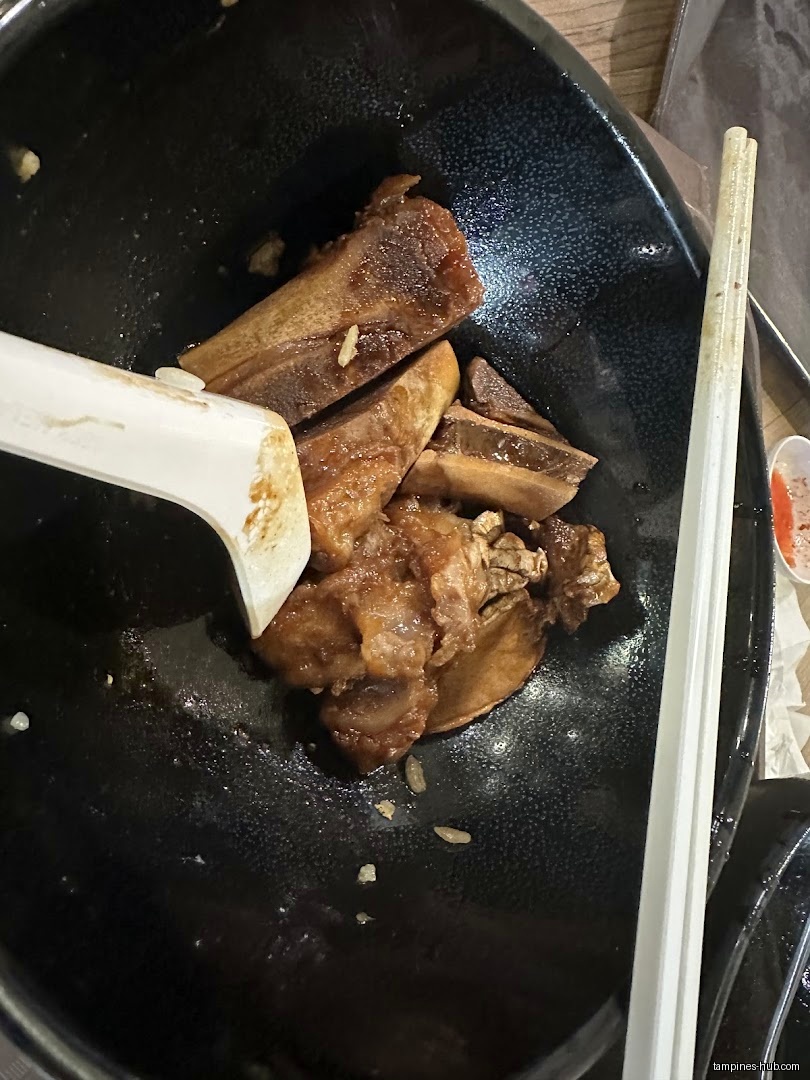 A black bowl contains leftover ribs, rice, and a spoon with chopsticks.