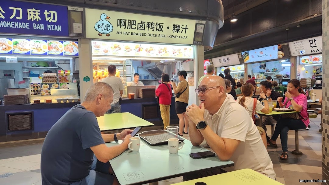People are eating at tables in a food court setting.