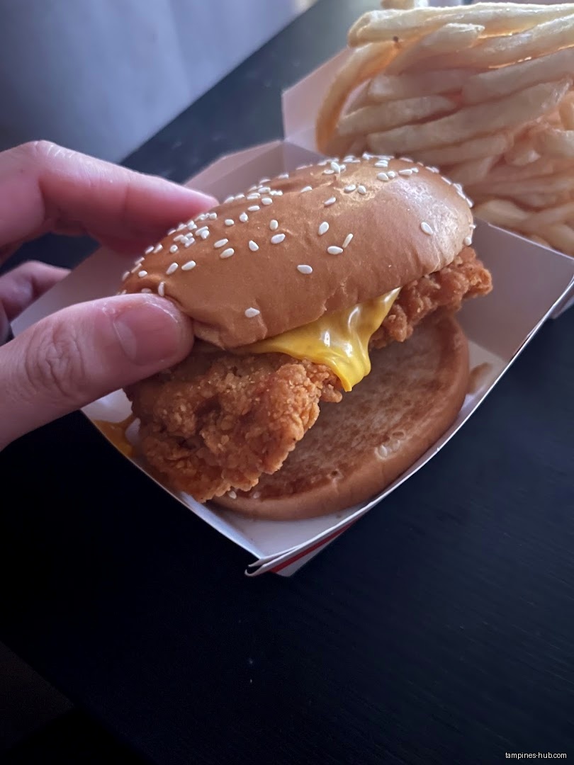 A hand holds a McDonald's chicken sandwich with fries in the background.