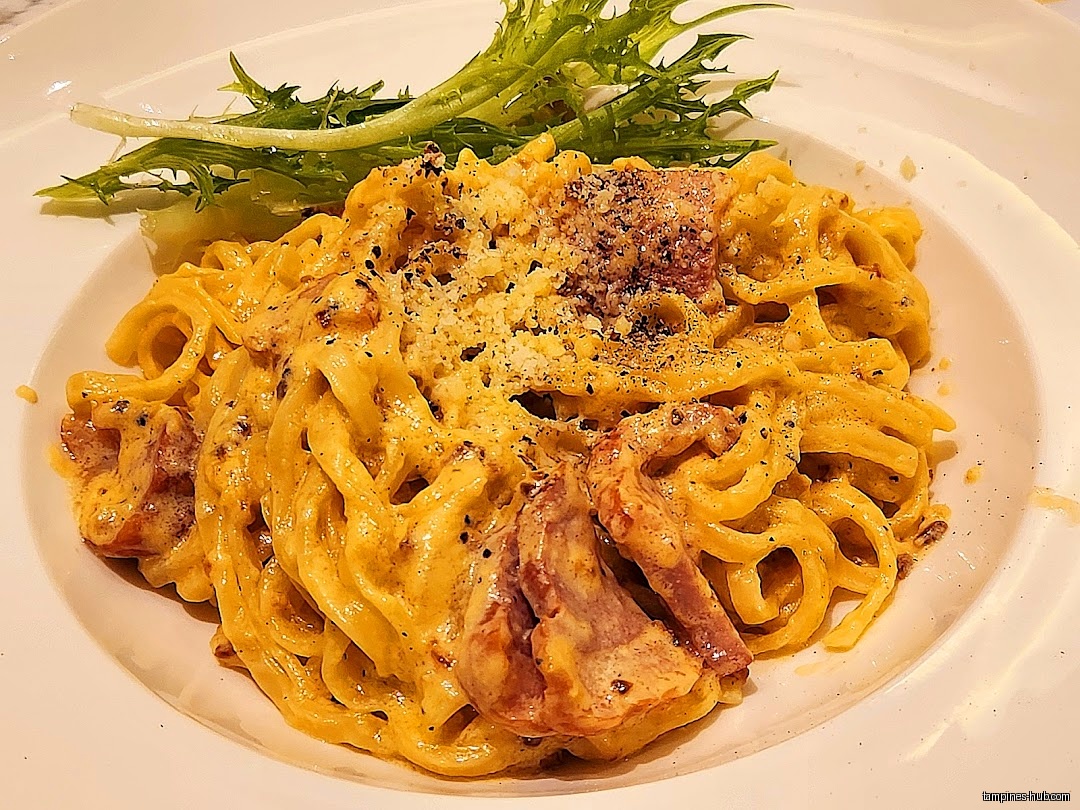 A plate of creamy pasta with meat and a side of greens.