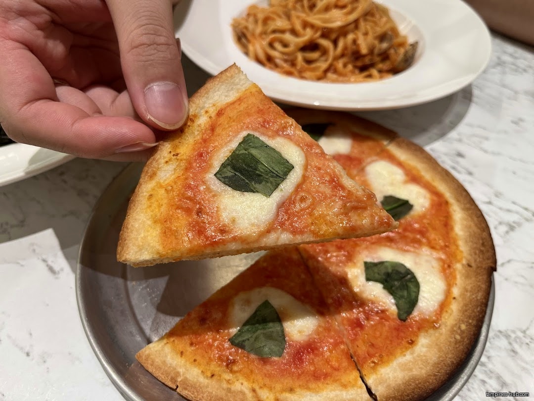 A hand holds a slice of pizza with a whole pizza and pasta.