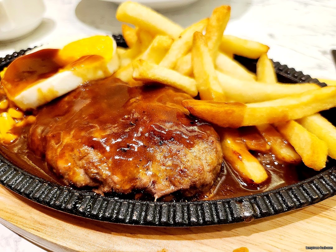 A sizzling plate with a hamburger steak, fries, and a halved egg.