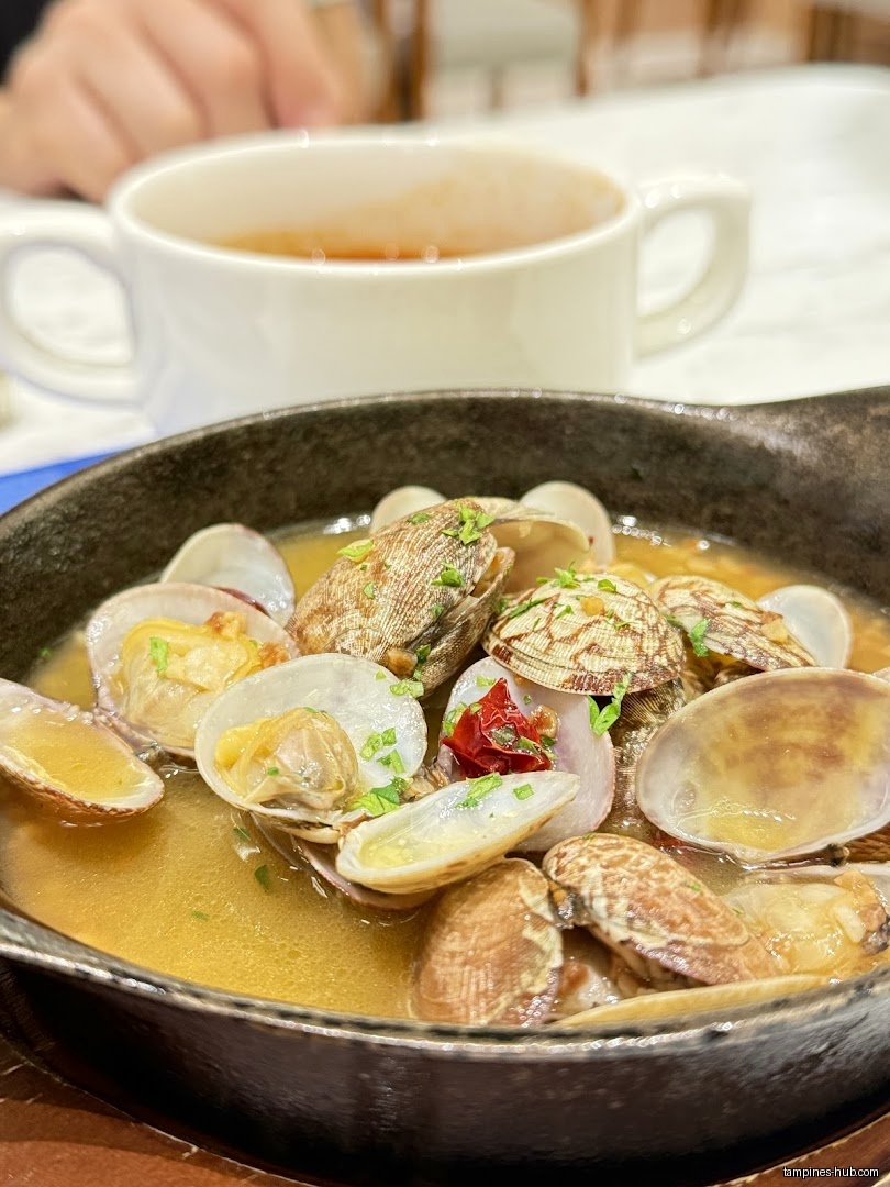 A bowl of clams in broth and a cup of soup on a table.