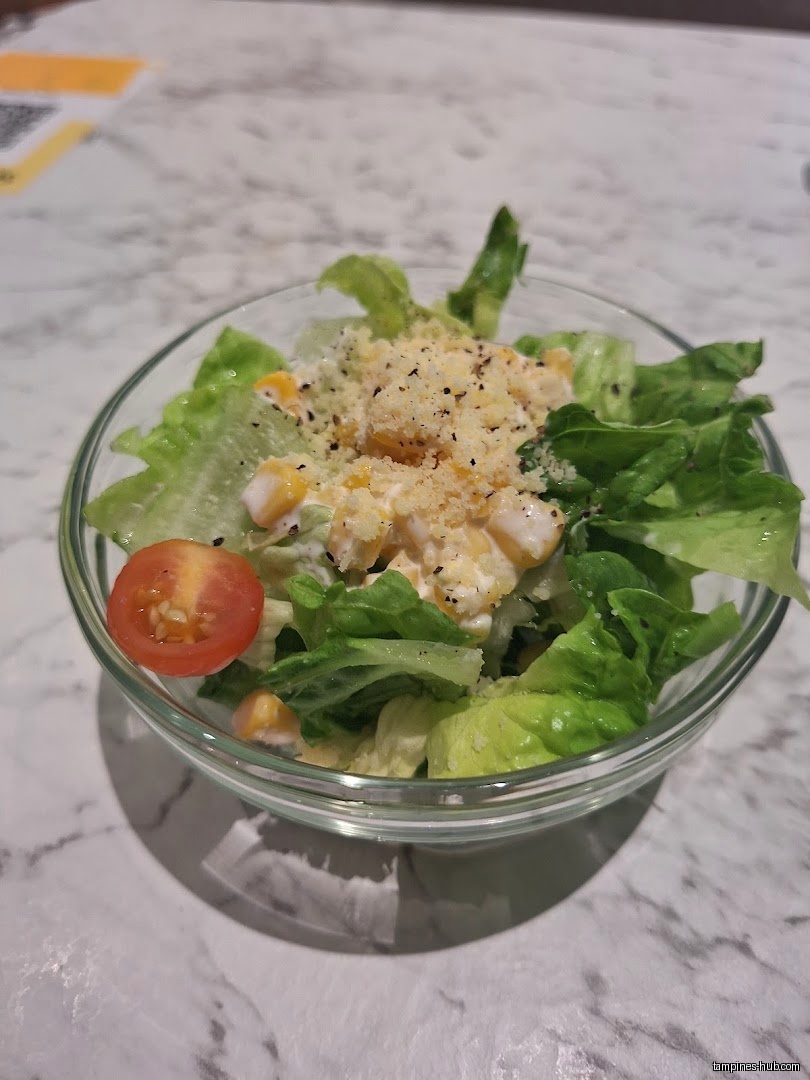 A small salad with lettuce, corn, tomato, and dressing in a glass bowl.
