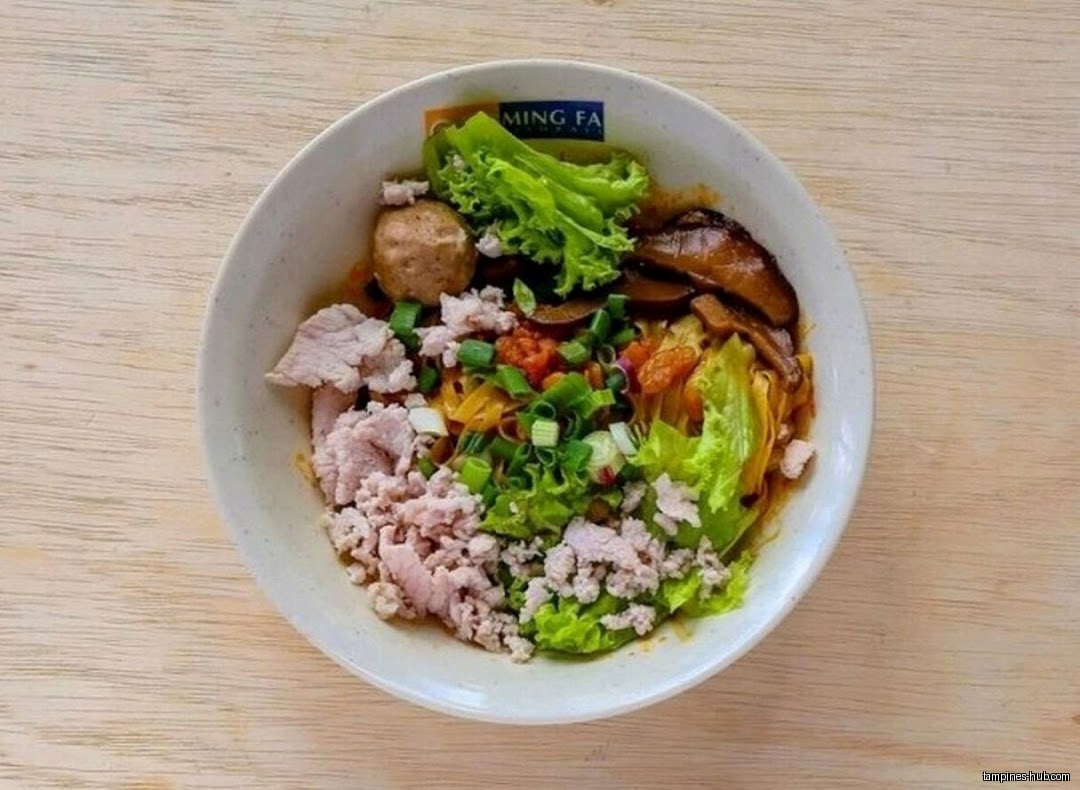 A bowl of noodles with meat, vegetables, and a fishball is shown.
