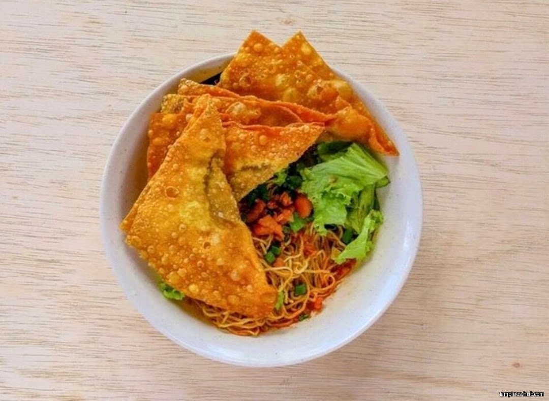 A bowl of noodles with fried wontons and lettuce is shown.