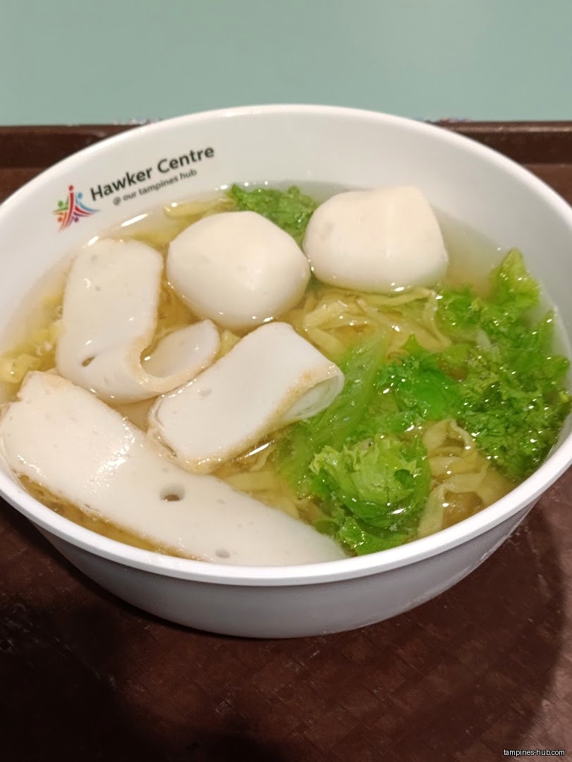 A bowl of fishball noodles with vegetables in broth.