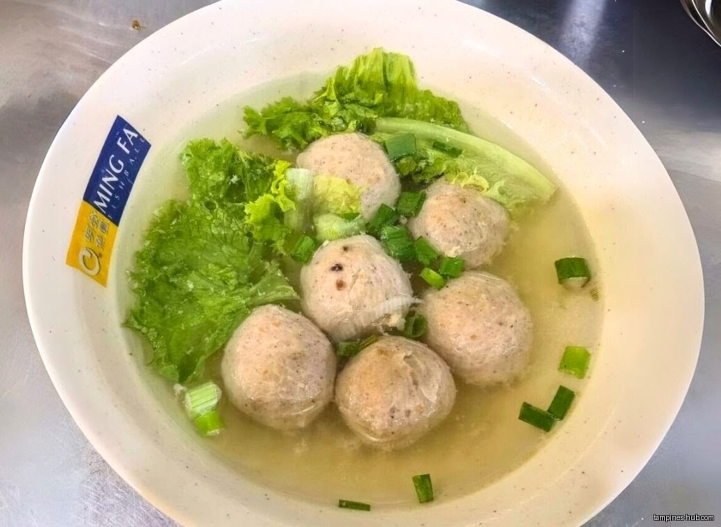 A bowl of Ming Fa Fishball soup with lettuce and green onions.