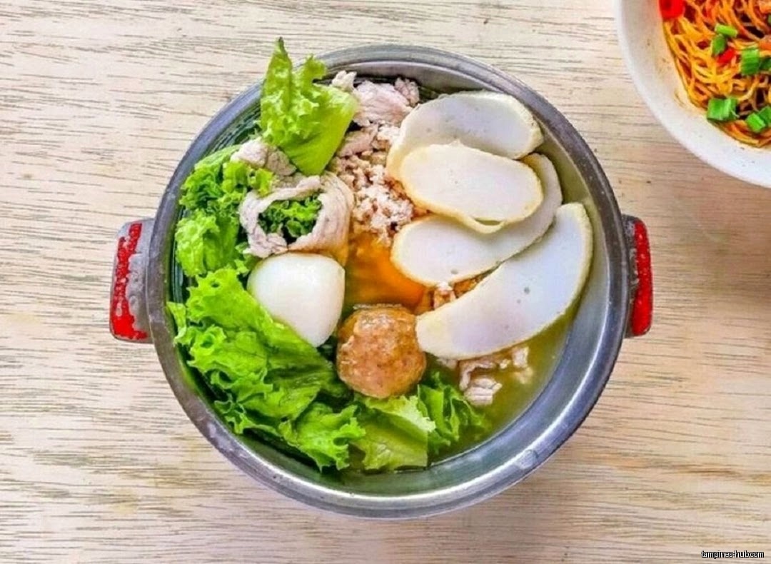 A bowl of fishball soup with lettuce, meat, and other ingredients.