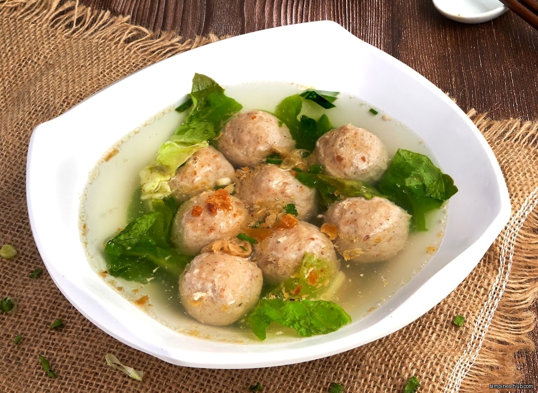 A bowl of fishball soup with leafy greens is presented on a table.