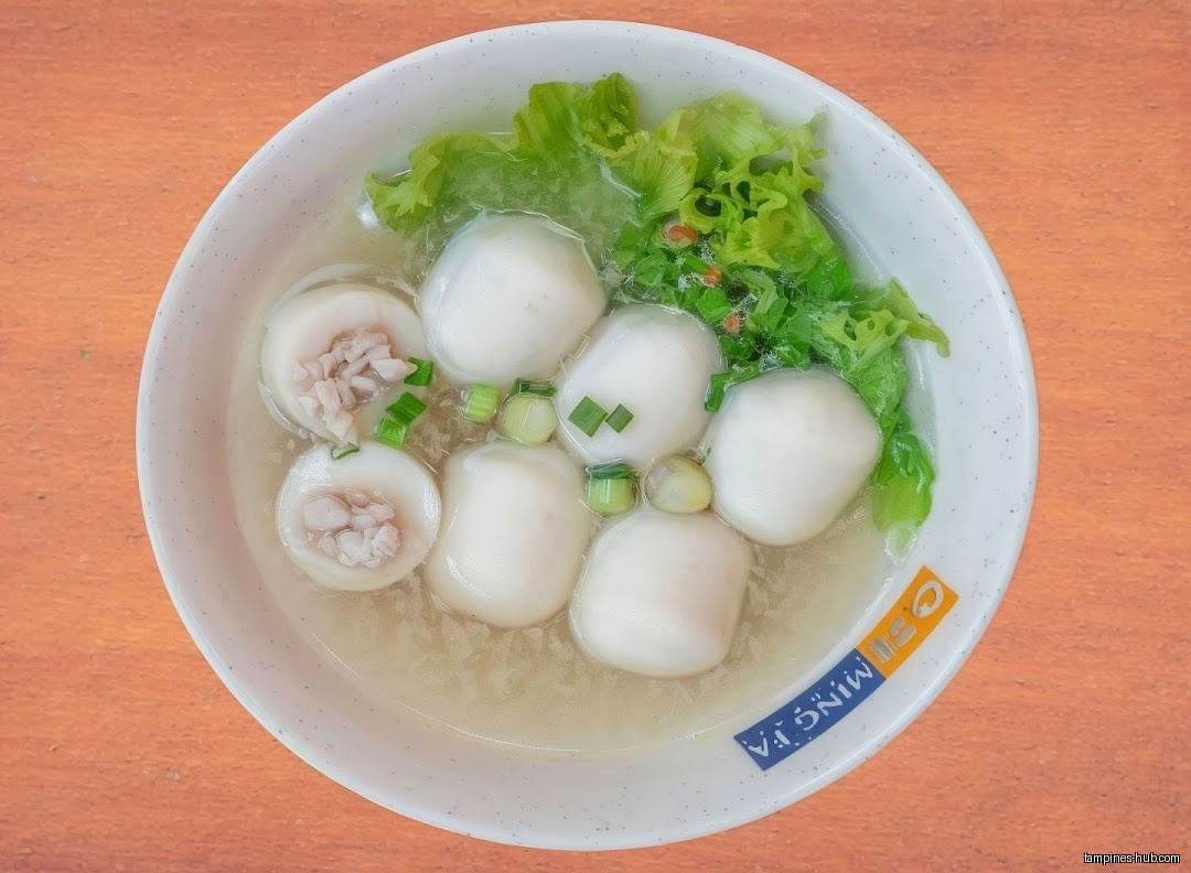 A bowl of fishball soup with lettuce and green onions is shown.