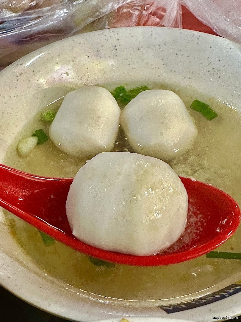 A bowl of fishball soup with a fishball on a red spoon.