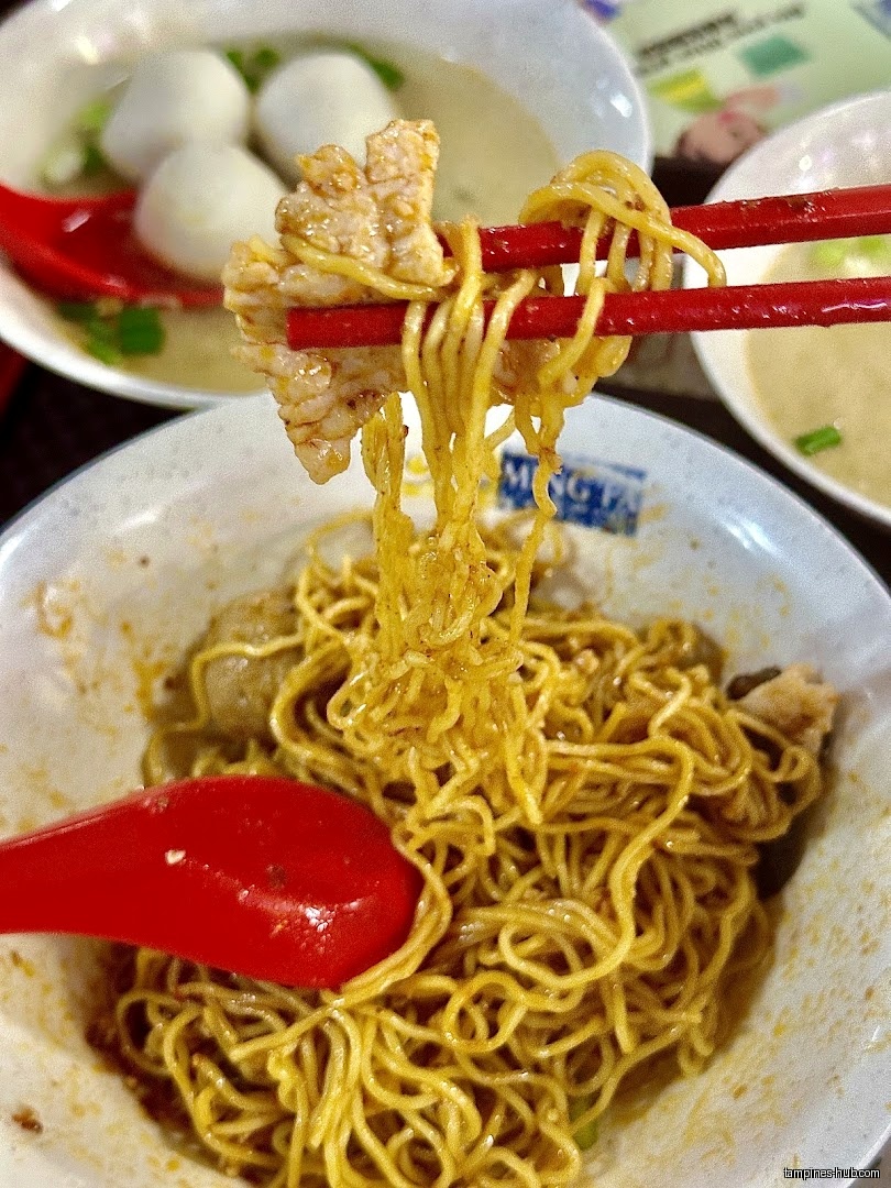 Close-up of yellow noodles with meat, held by red chopsticks, and red spoon.