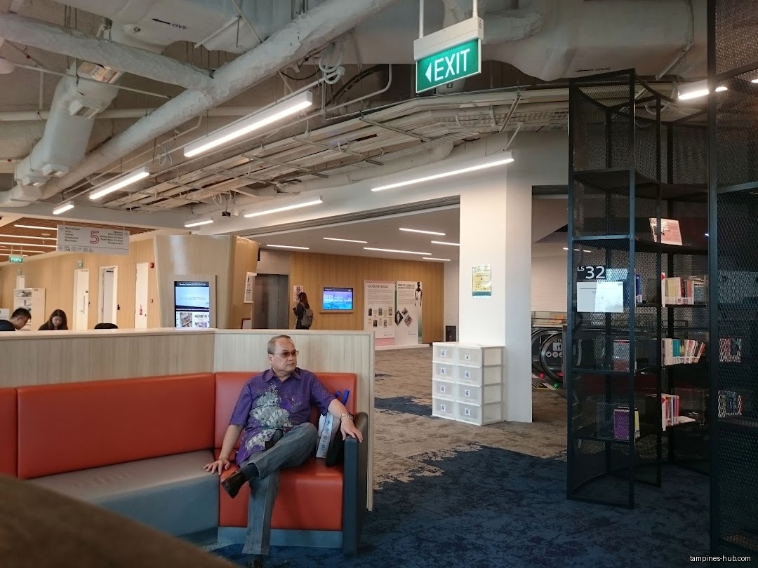 Man sits on a couch in a public space with bookshelves.