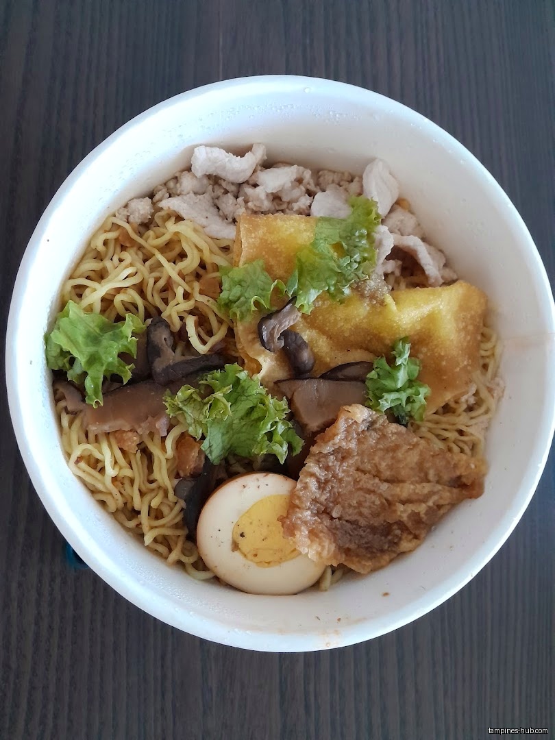 A bowl of noodles with egg, mushrooms, fried wonton, and meat.