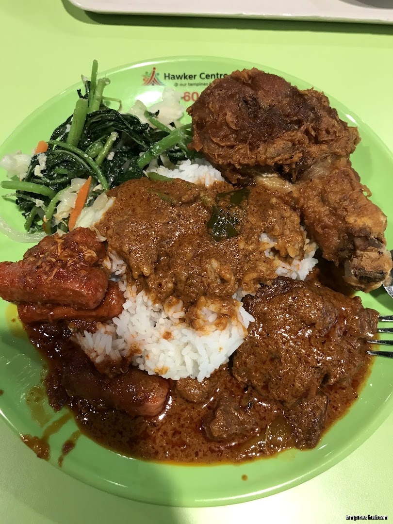 A plate of rice with rendang, fried chicken, and vegetables is shown.