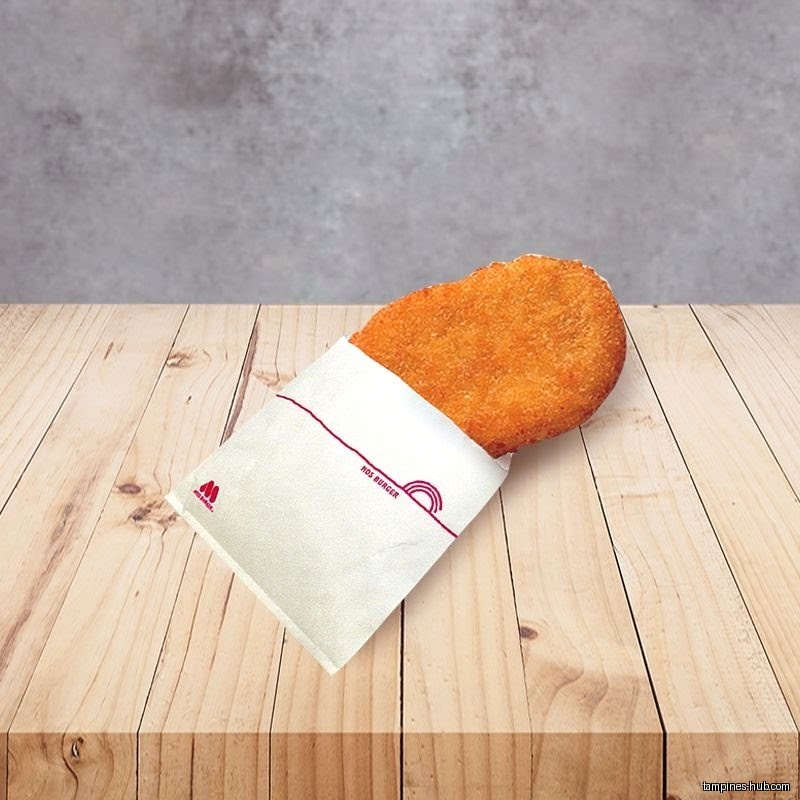 A MOS Burger hash brown in its wrapper sits on a wooden table.