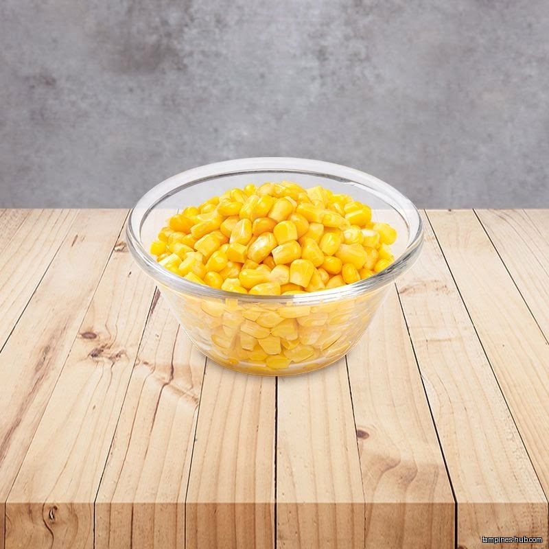 A clear bowl filled with yellow corn kernels sits on a wooden table.