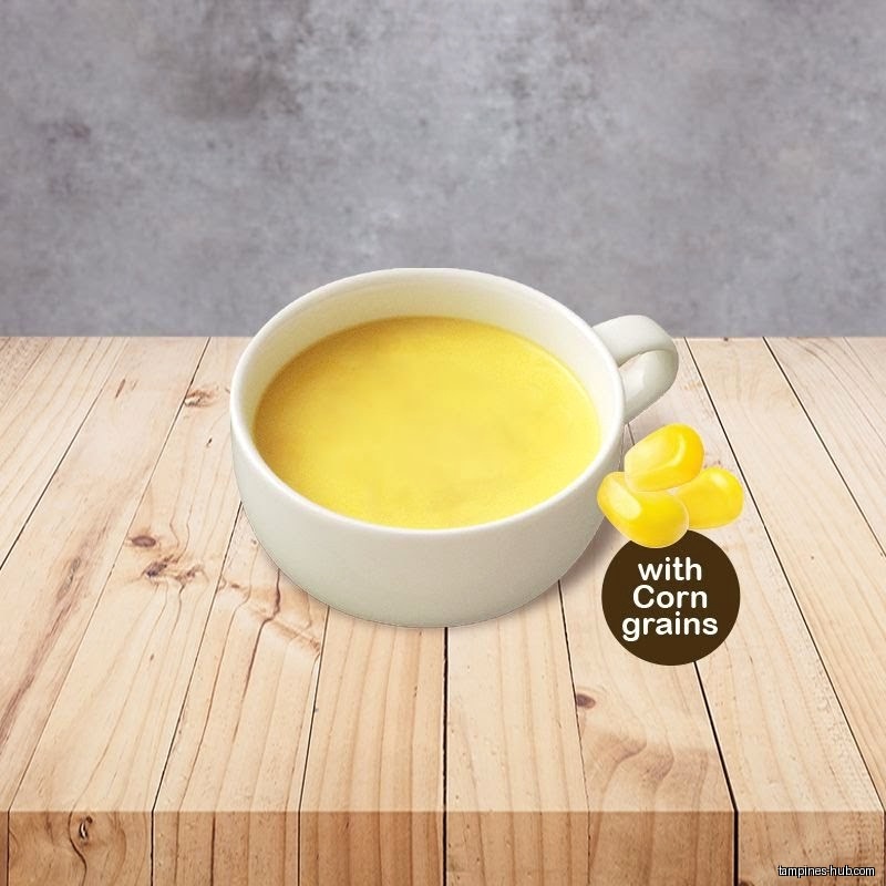 A cup of corn soup with corn grains on a wooden table.