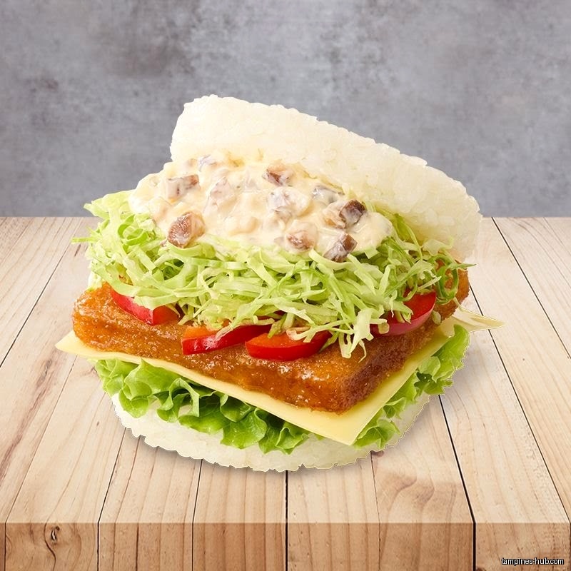 A rice burger with fish, cheese, lettuce, and sauce sits on a table.