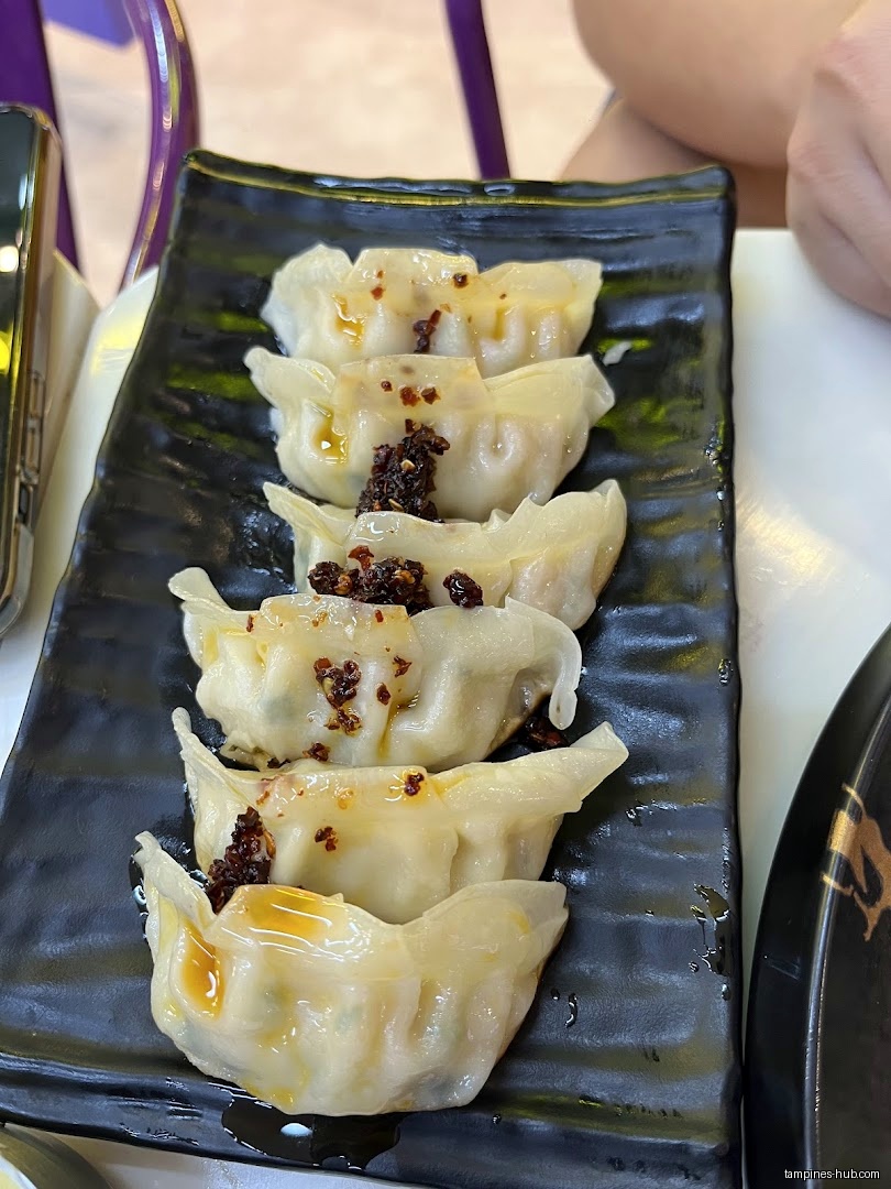 A black plate holds six dumplings topped with chili oil and flakes.