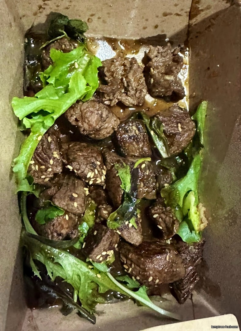 A takeout box filled with beef cubes and green lettuce.