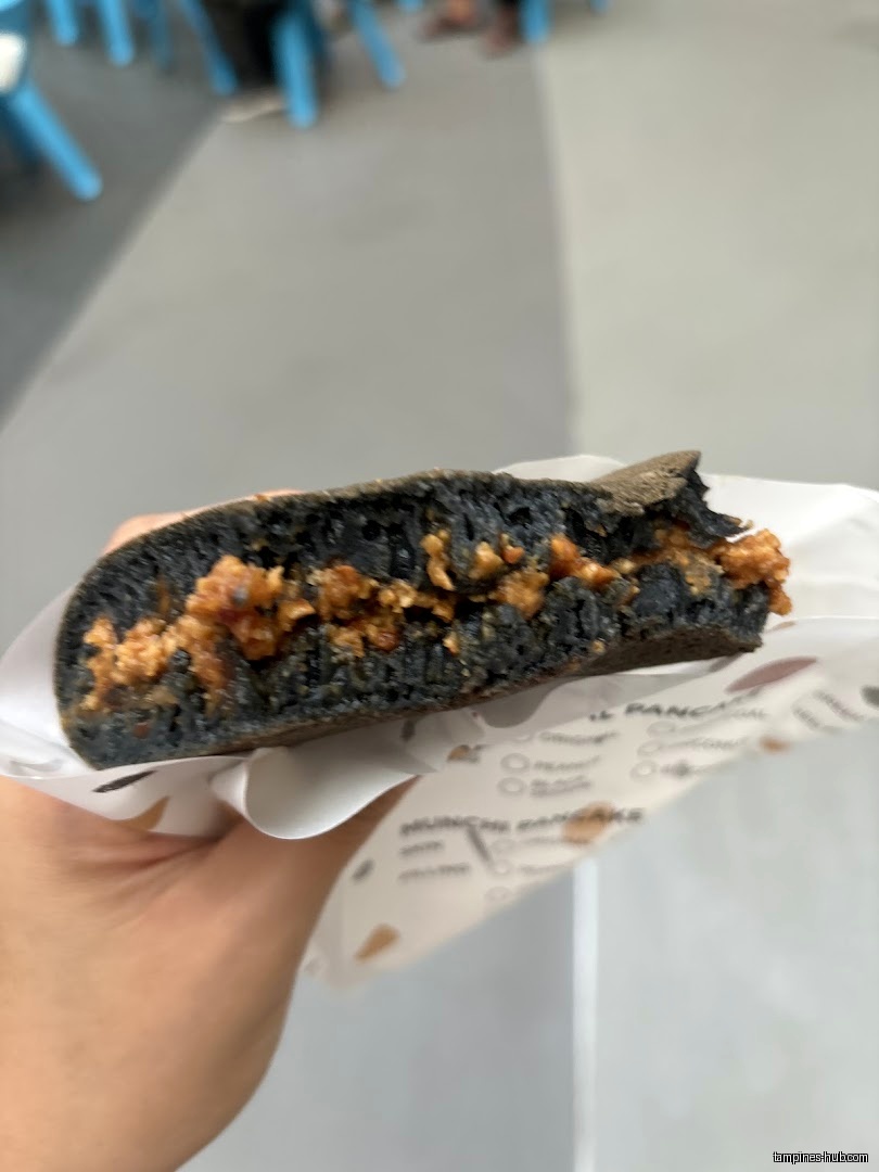 A hand holds a cut black pancake with filling from Munchi Pancakes.
