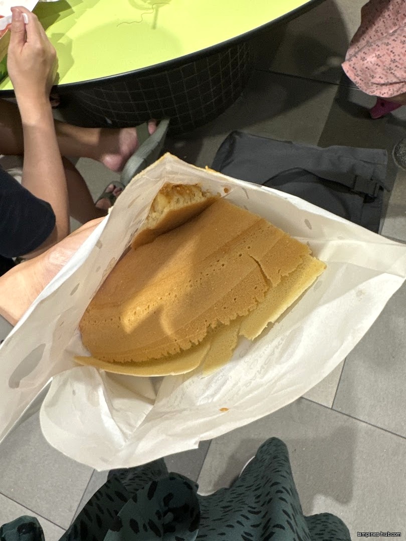 A Munchi Pancake in a paper bag, near a table and people.