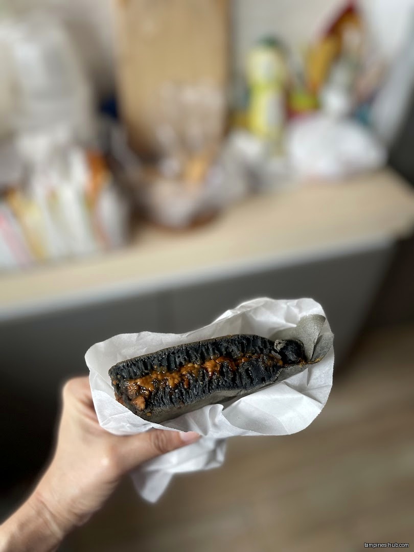 A hand holds a dark pancake with a filling in white paper.