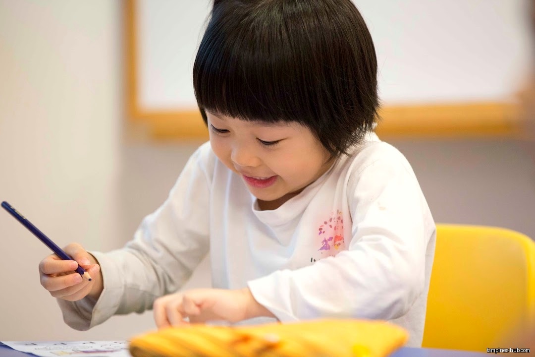 A young girl is drawing with a colored pencil at a desk.