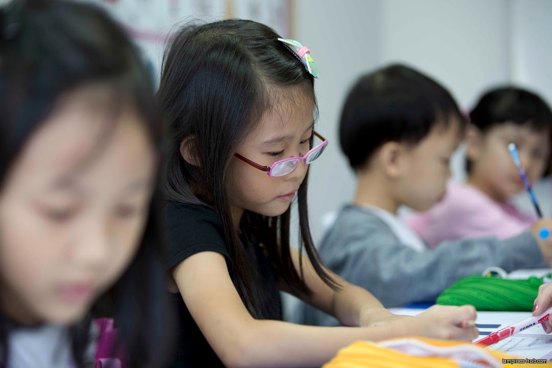 Children are sitting at desks and writing in a classroom setting.