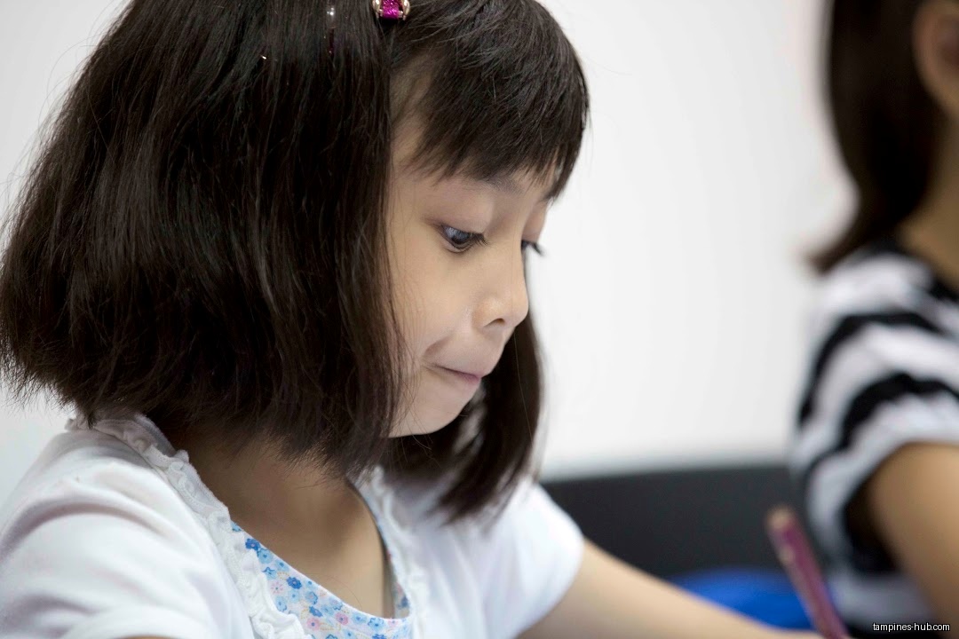 A young girl with dark hair is looking down and writing.