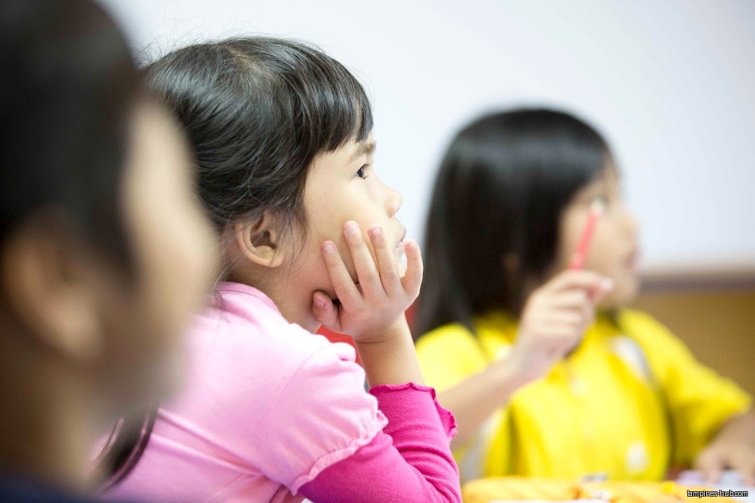 Three young students are in a classroom setting, looking to the side.