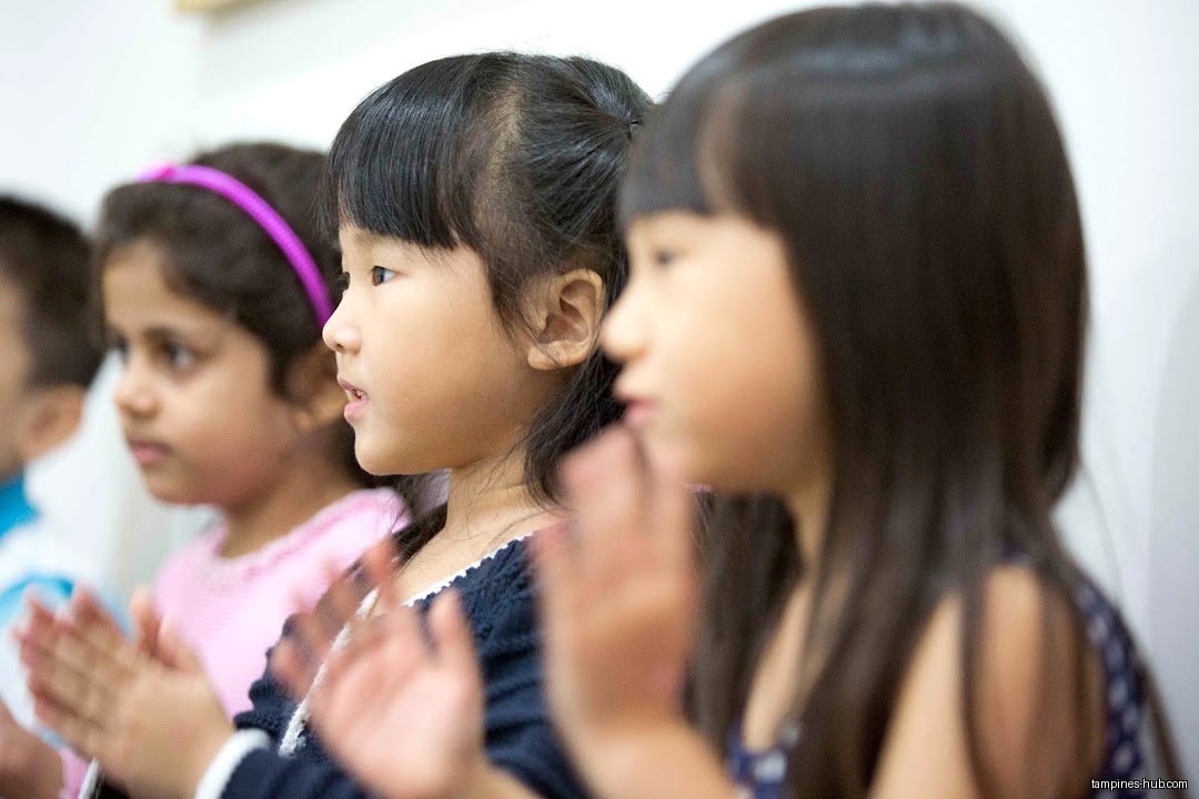 A group of young children are clapping their hands in a classroom.