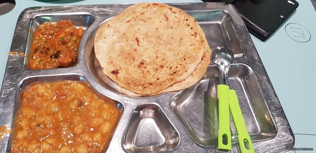 A metal tray holds roti, curry, and chana masala, with utensils.