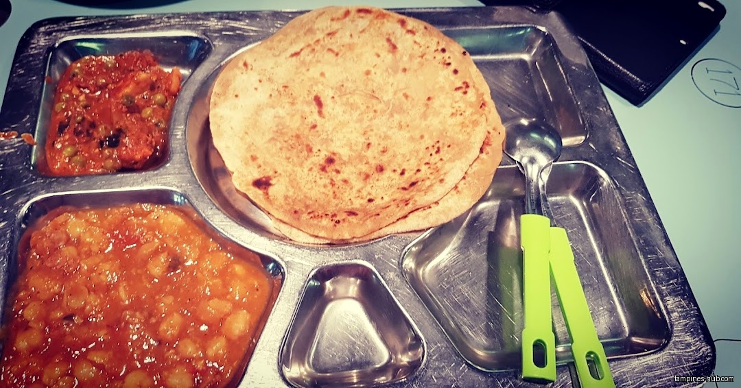 A metal tray with roti, vegetables, and a spoon is shown.