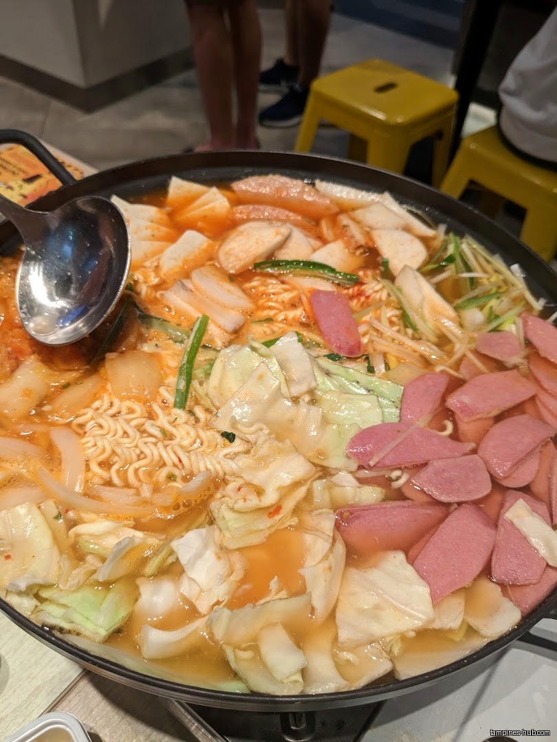 A pot of Korean stew with noodles, cabbage, and sliced sausage.