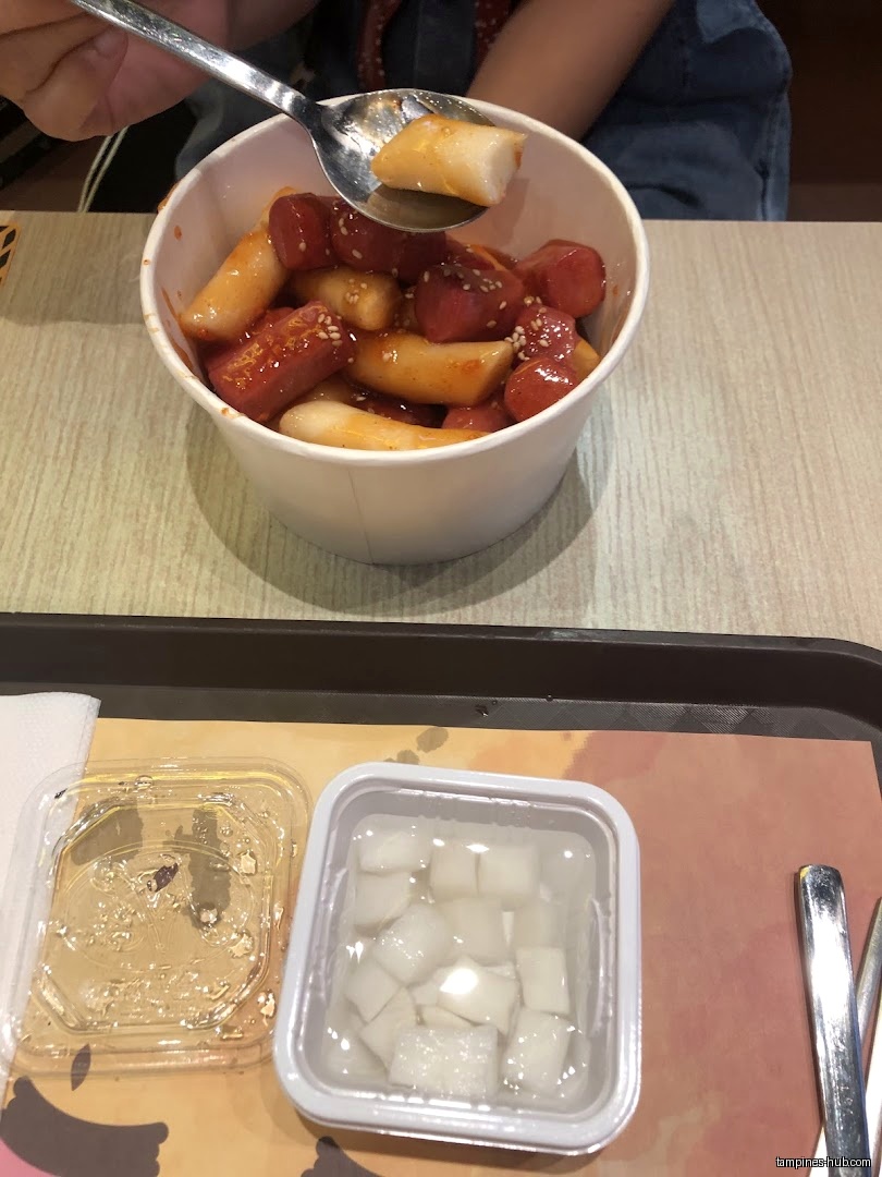 A bowl of tteokbokki with sausages and side dishes on a tray.