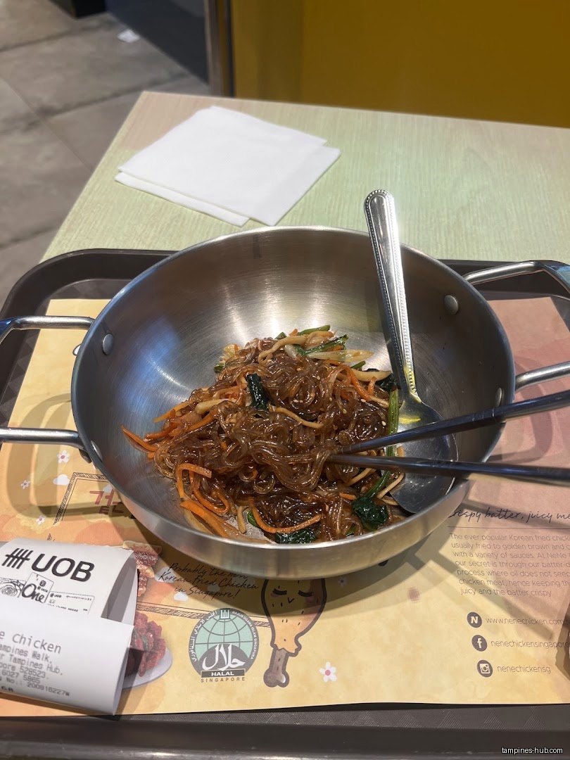 Japchae noodles in a metal bowl with chopsticks and a spoon.