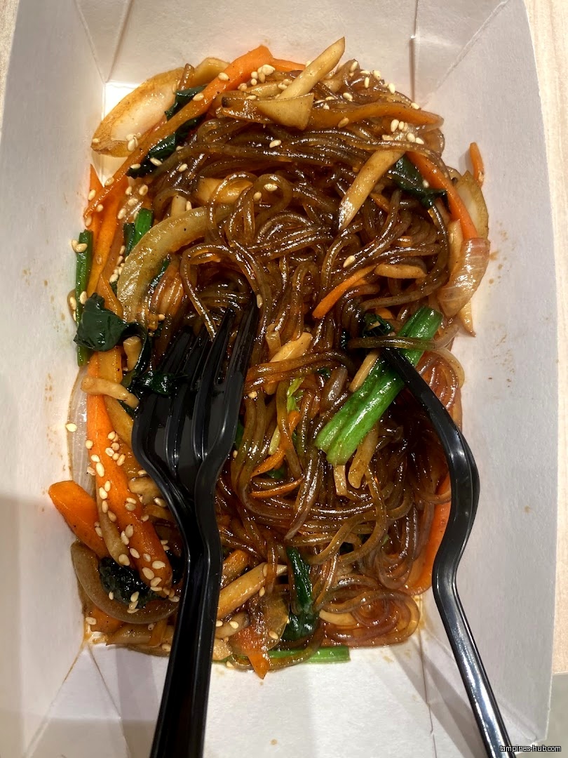 A box of Japchae noodles with vegetables and two black forks.