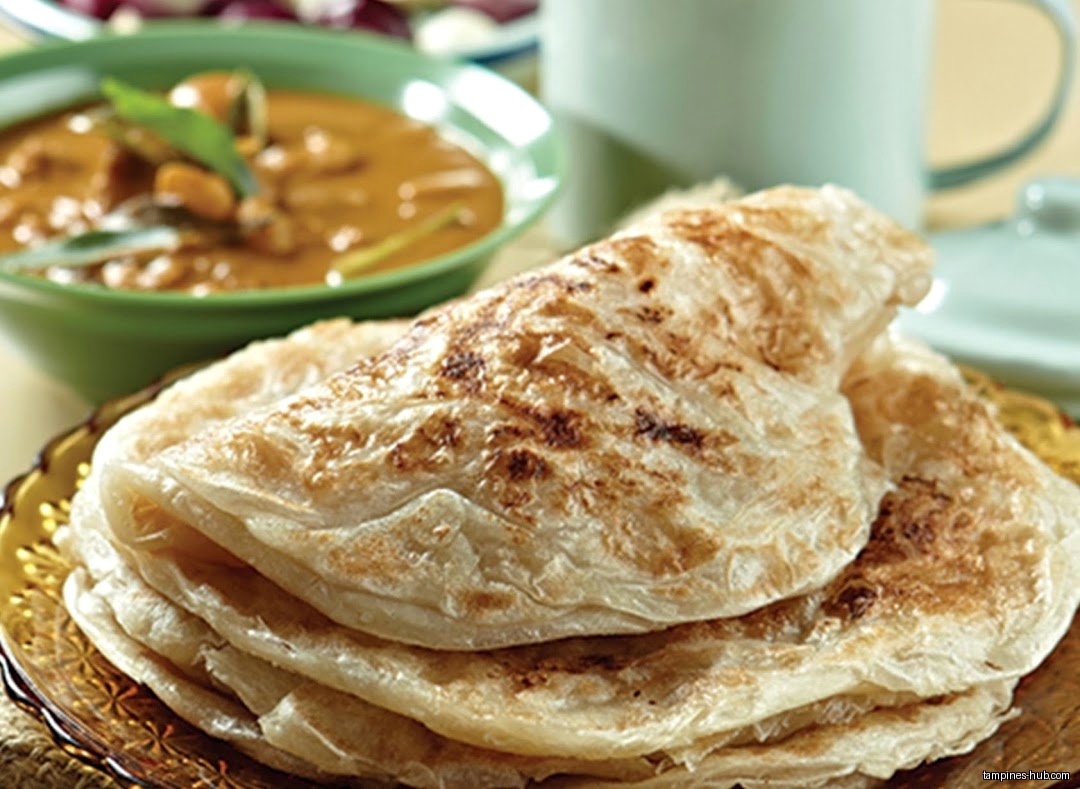 A stack of roti prata sits next to a bowl of curry.