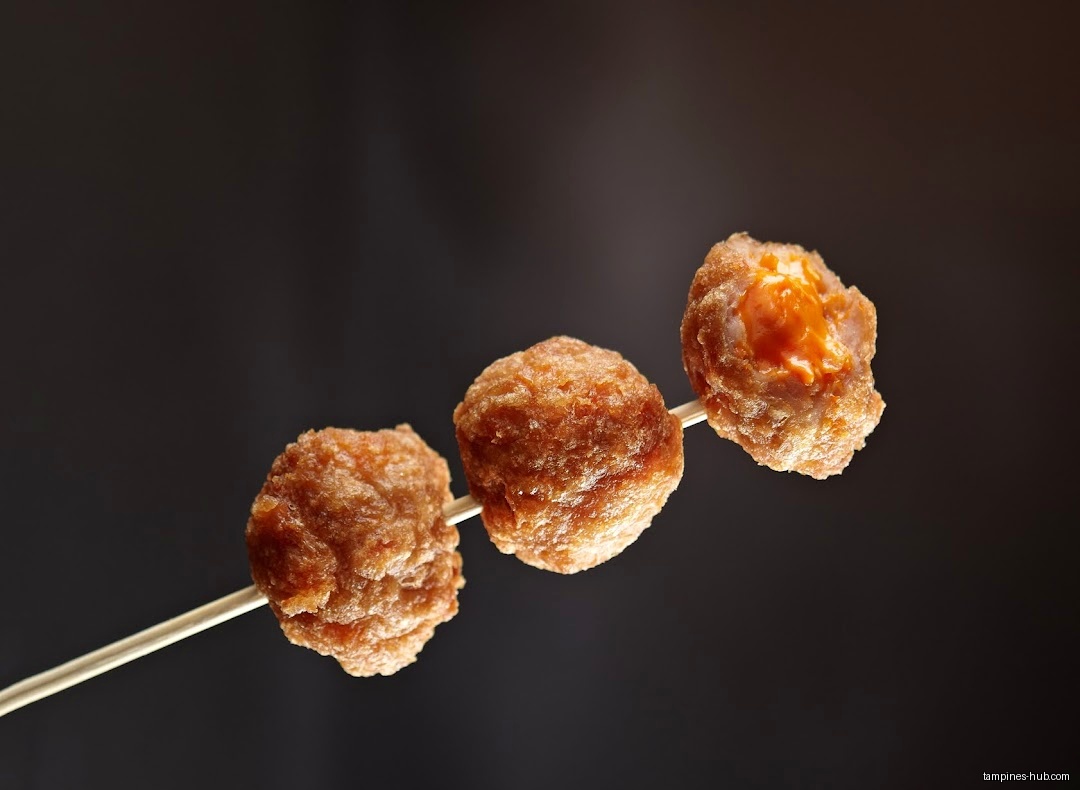 Three fried balls on a stick, one with orange filling.