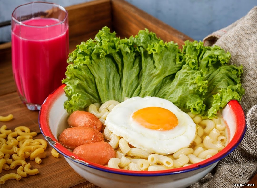 A bowl of macaroni with egg, sausage, lettuce, and a pink drink.