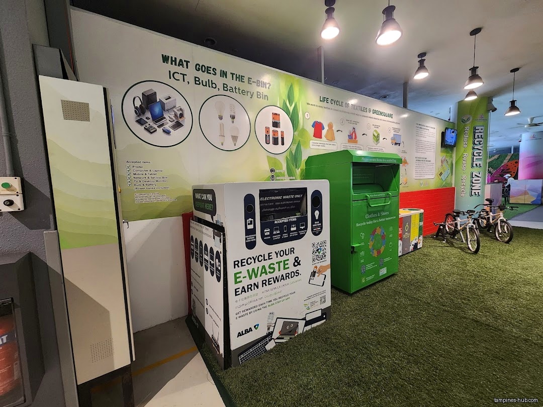 The image shows an indoor recycling zone with bins and informational posters.